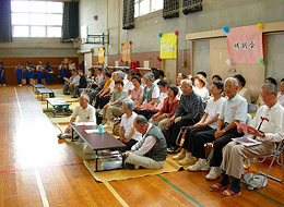 体育館の中でたくさんの人たちが座っている写真