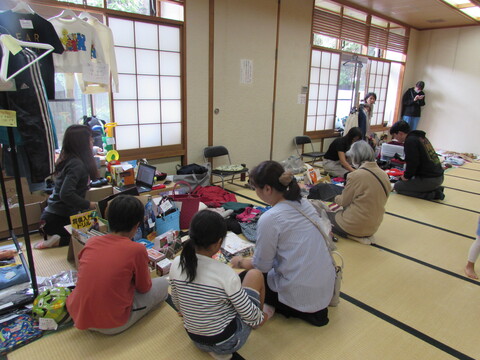 畳の上に座っている人々と、衣類等が置かれた和室の中の写真