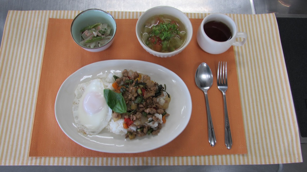 オレンジ色のランチョンマットに乗せられた、ガパオライスと旬野菜のメニューの写真