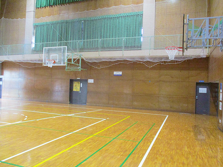 バスケットゴールがあり2階部分にネットが掛けられた体育館の写真