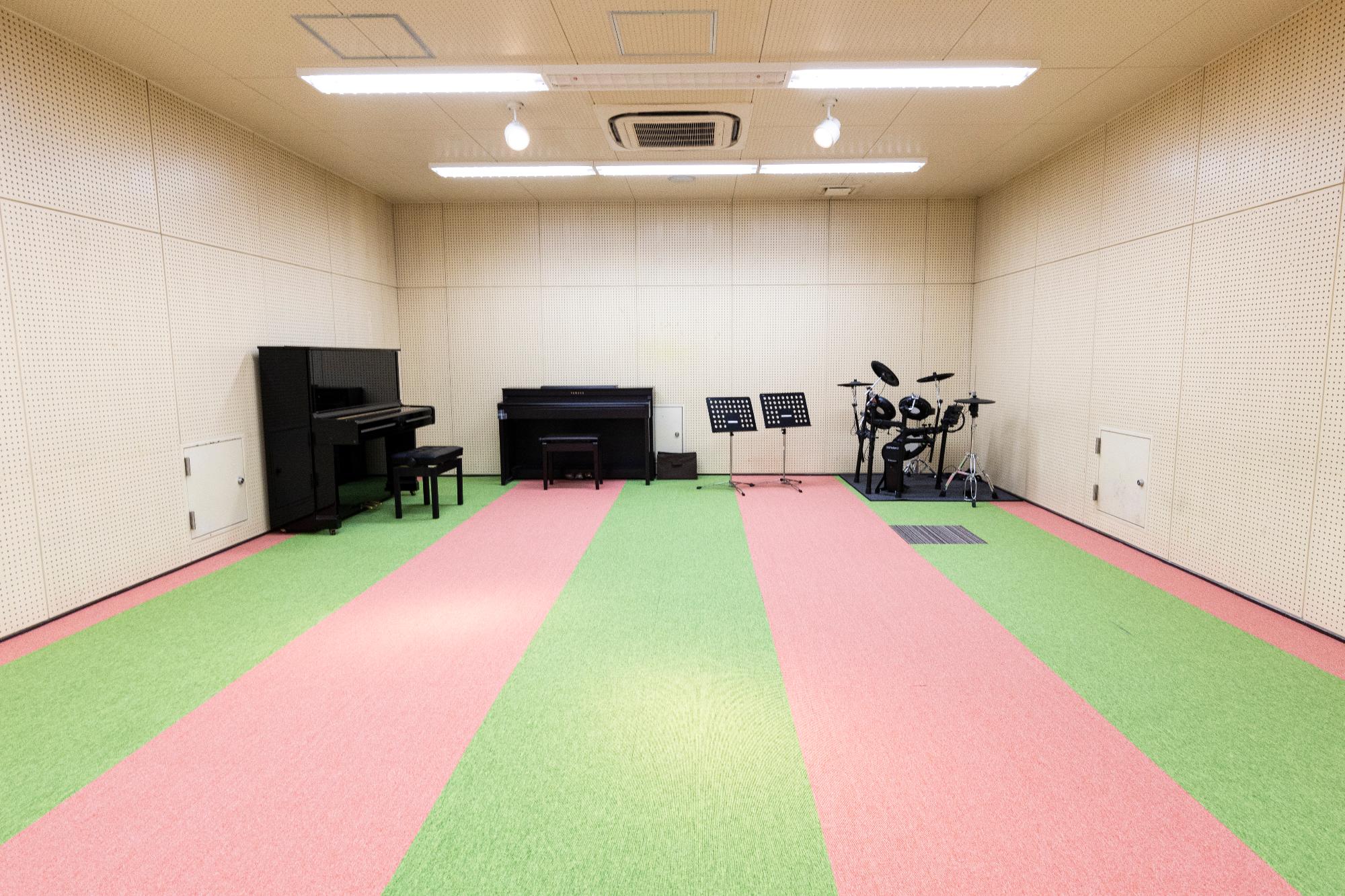 ドラムセットとピアノと譜面台が置いてあるピンクと黄緑色のじゅうたんの部屋の写真