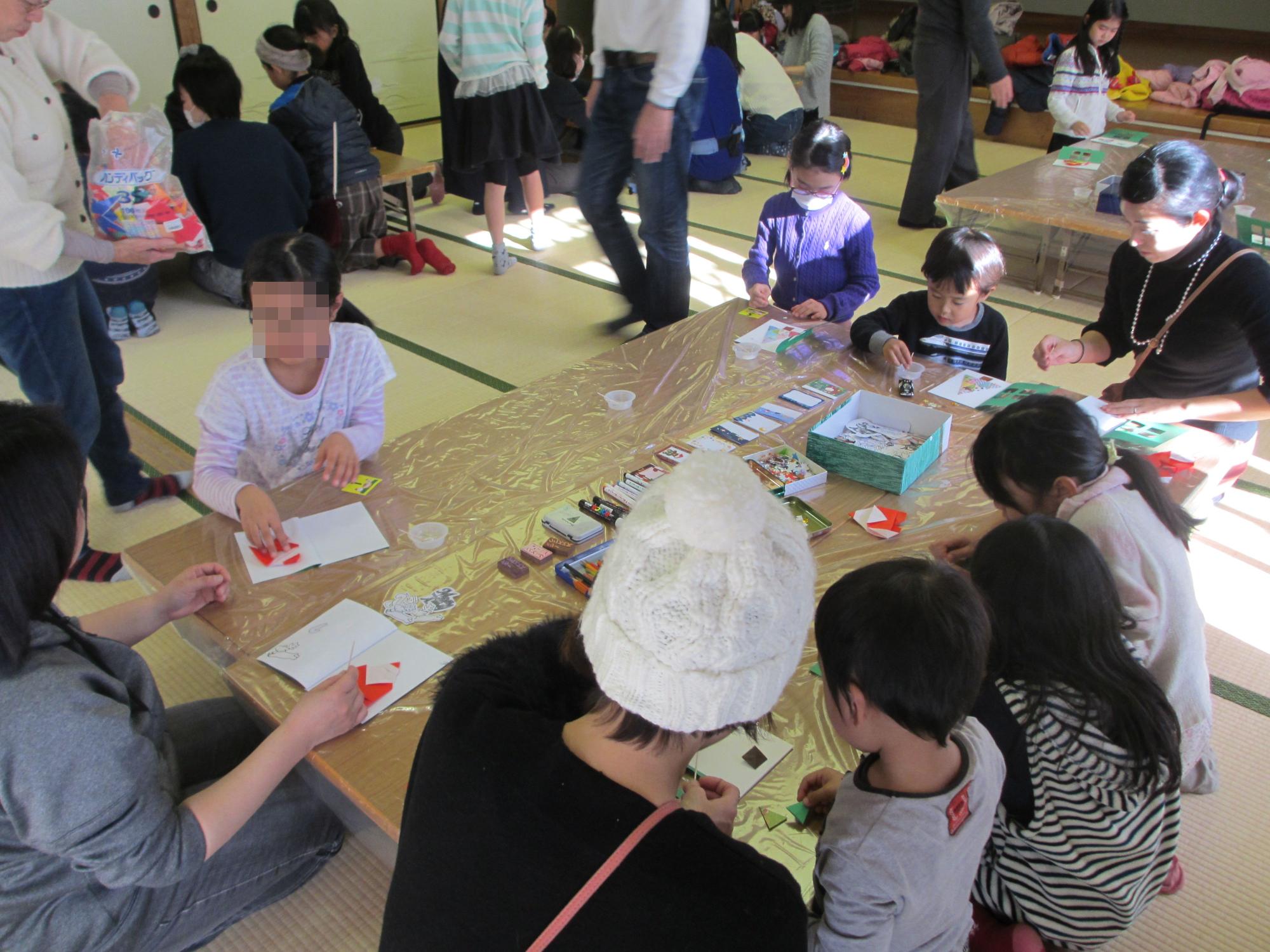 和室に座りながら、机の上に置かれた折り紙を折る子ども達の写真