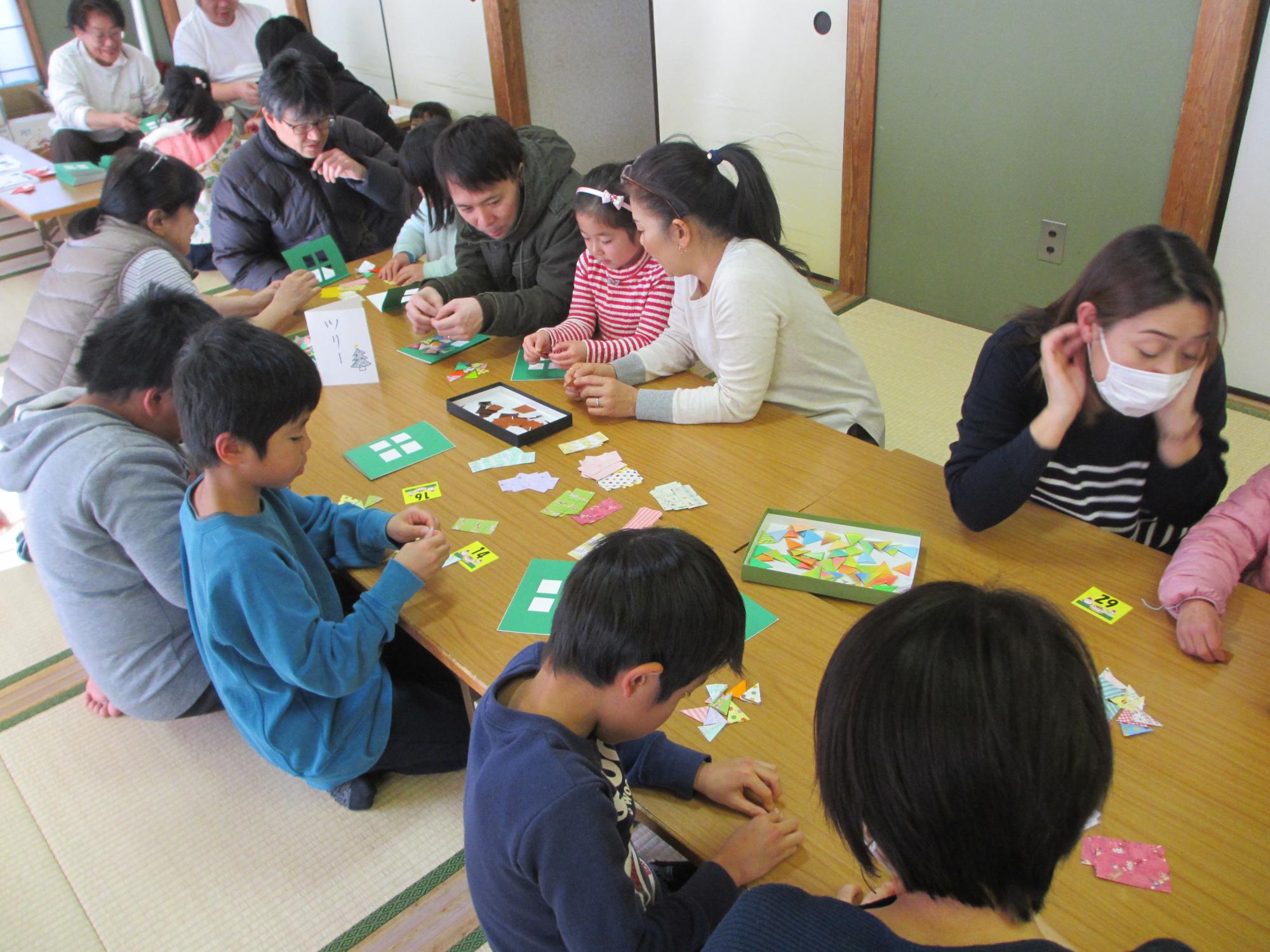 和室で座りながら、紙を貼り付けてカードを作る子供たちの写真