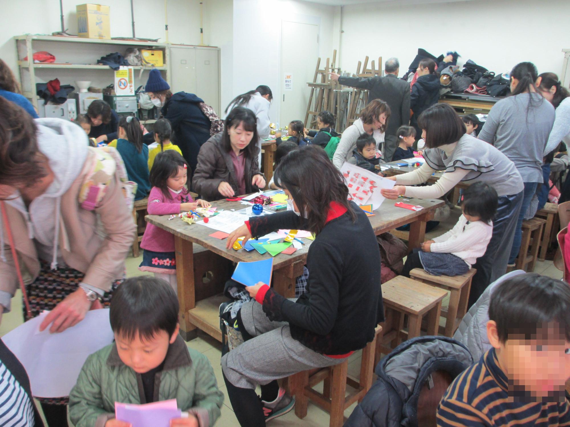 折り紙を折る大勢の子供たちと大人が集まっている写真