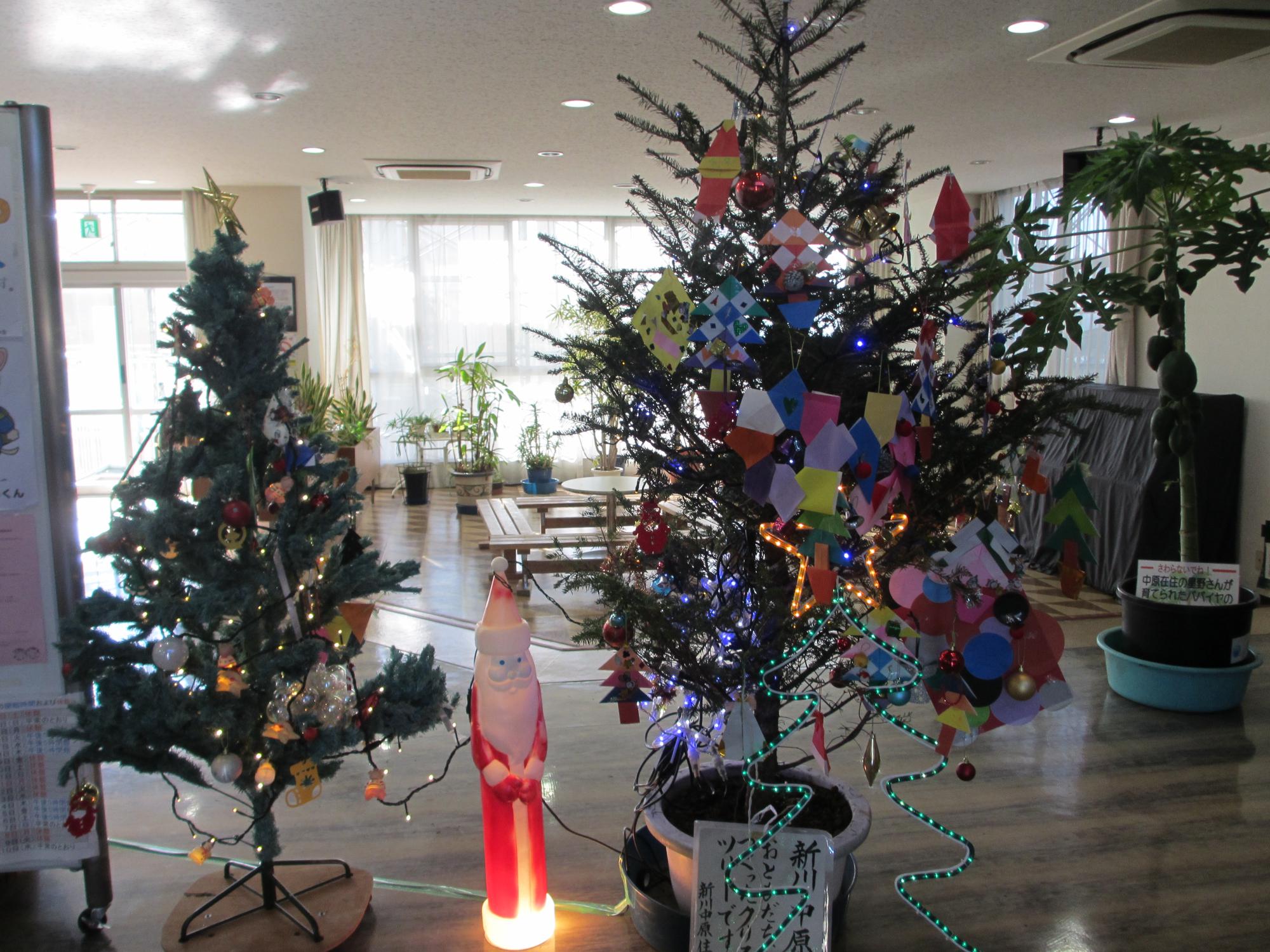 クリスマスツリーと大きなクリスマスツリーの中央に、小さなサンタクロースの光る人形が並べられている写真