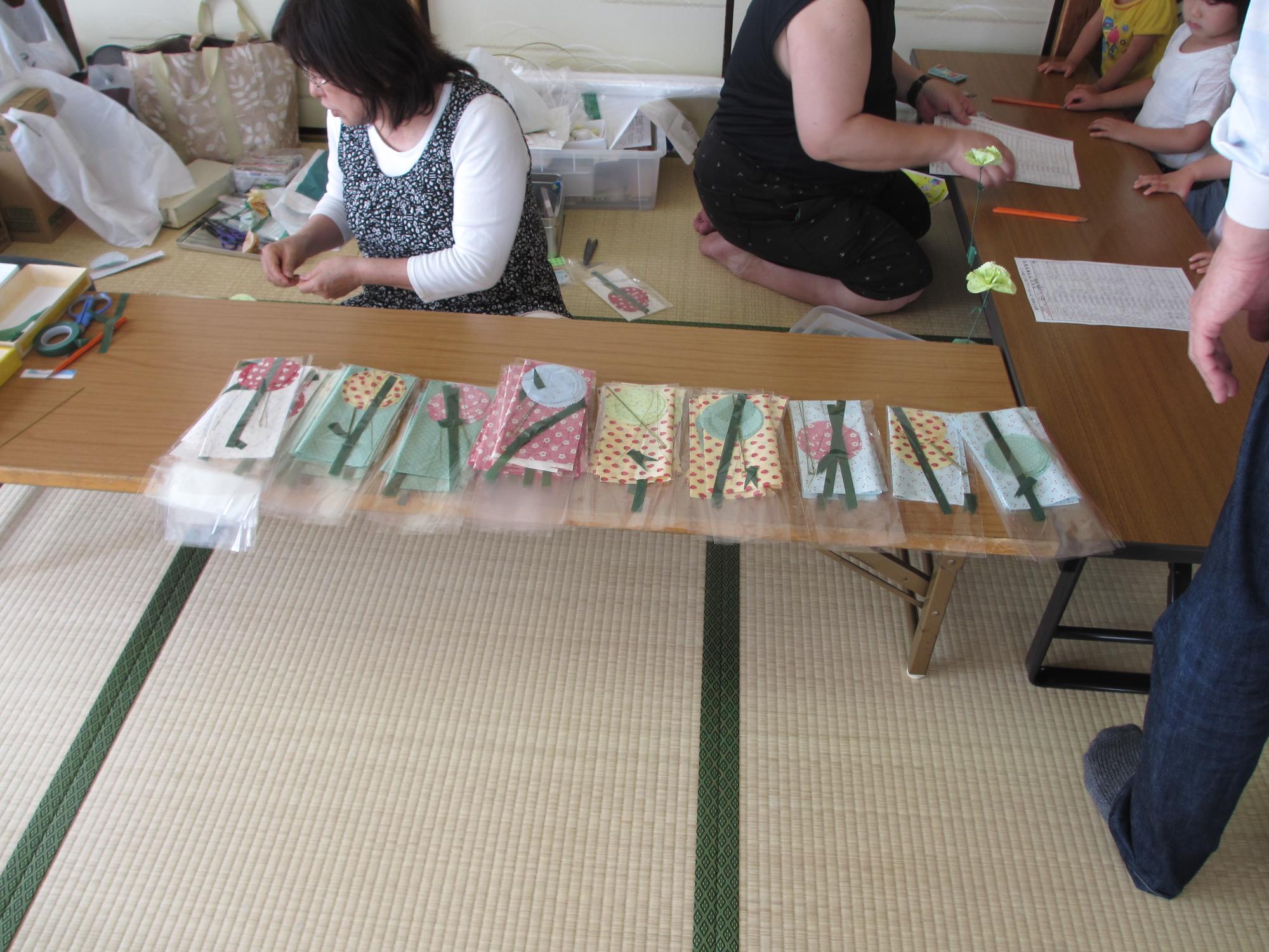 机の上に、花の折り紙が貼られた多くの袋が並べられている写真