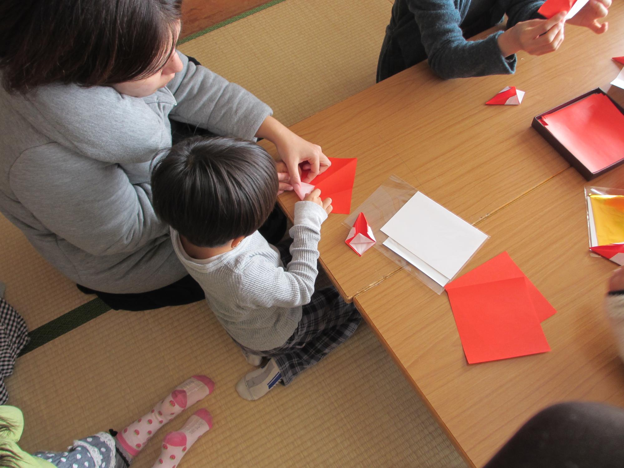 大人とともに折り紙を折る子供の写真