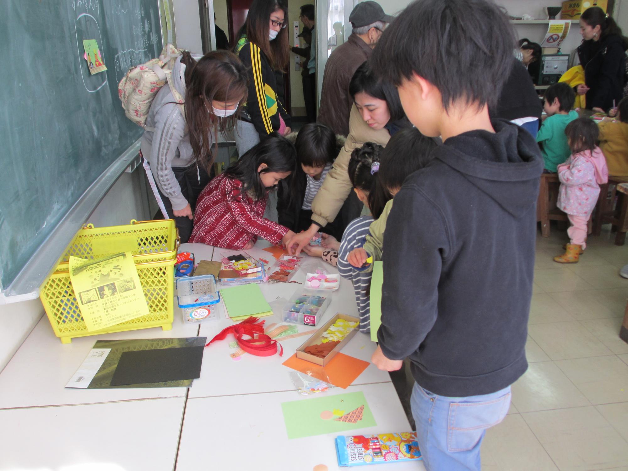 机の上で、紙を貼って遊んでいる子ども達と見守る保護者達の写真