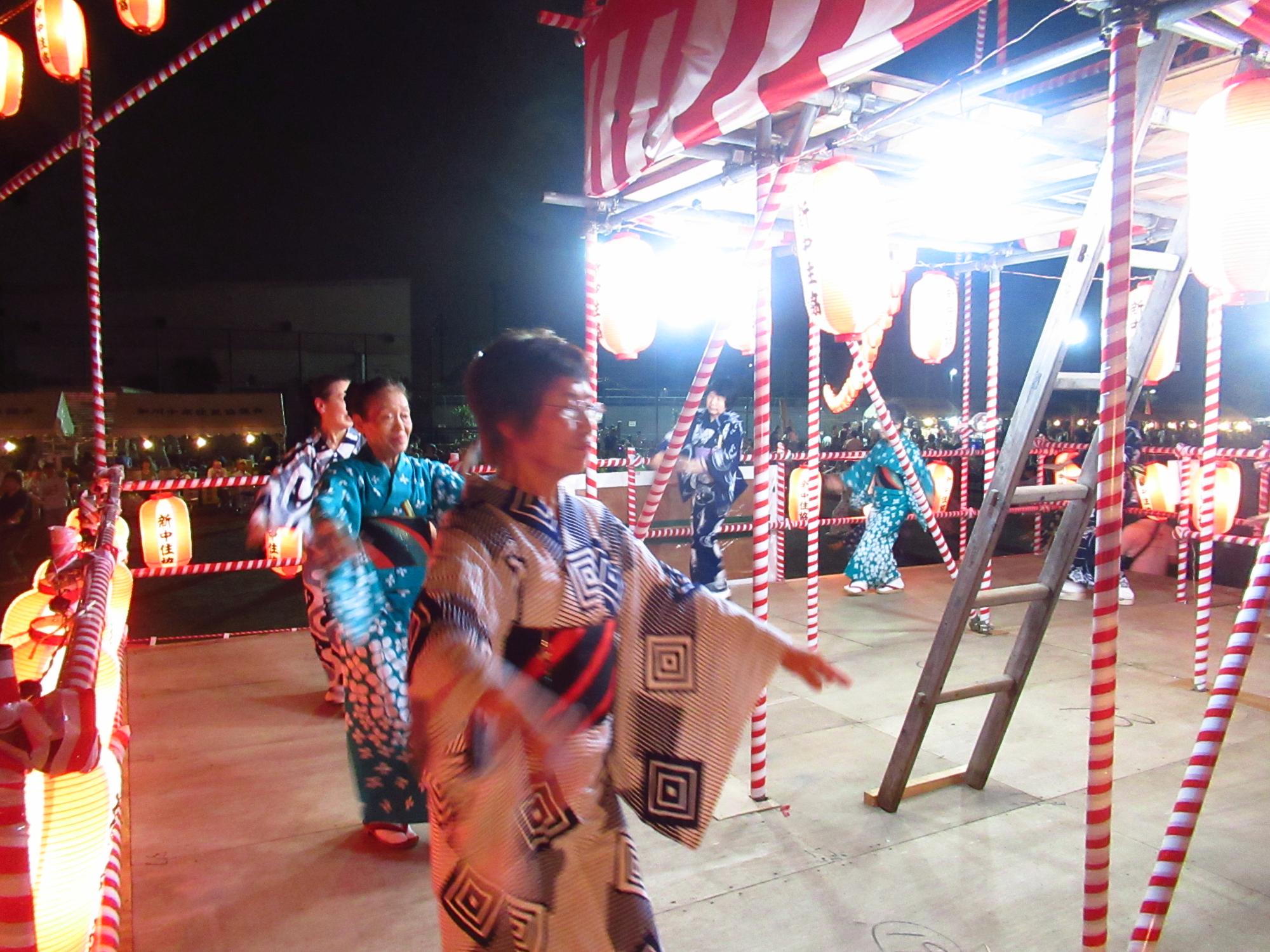 夜にやぐらに上がり、盆踊りを楽しむ着物を着た人々の写真