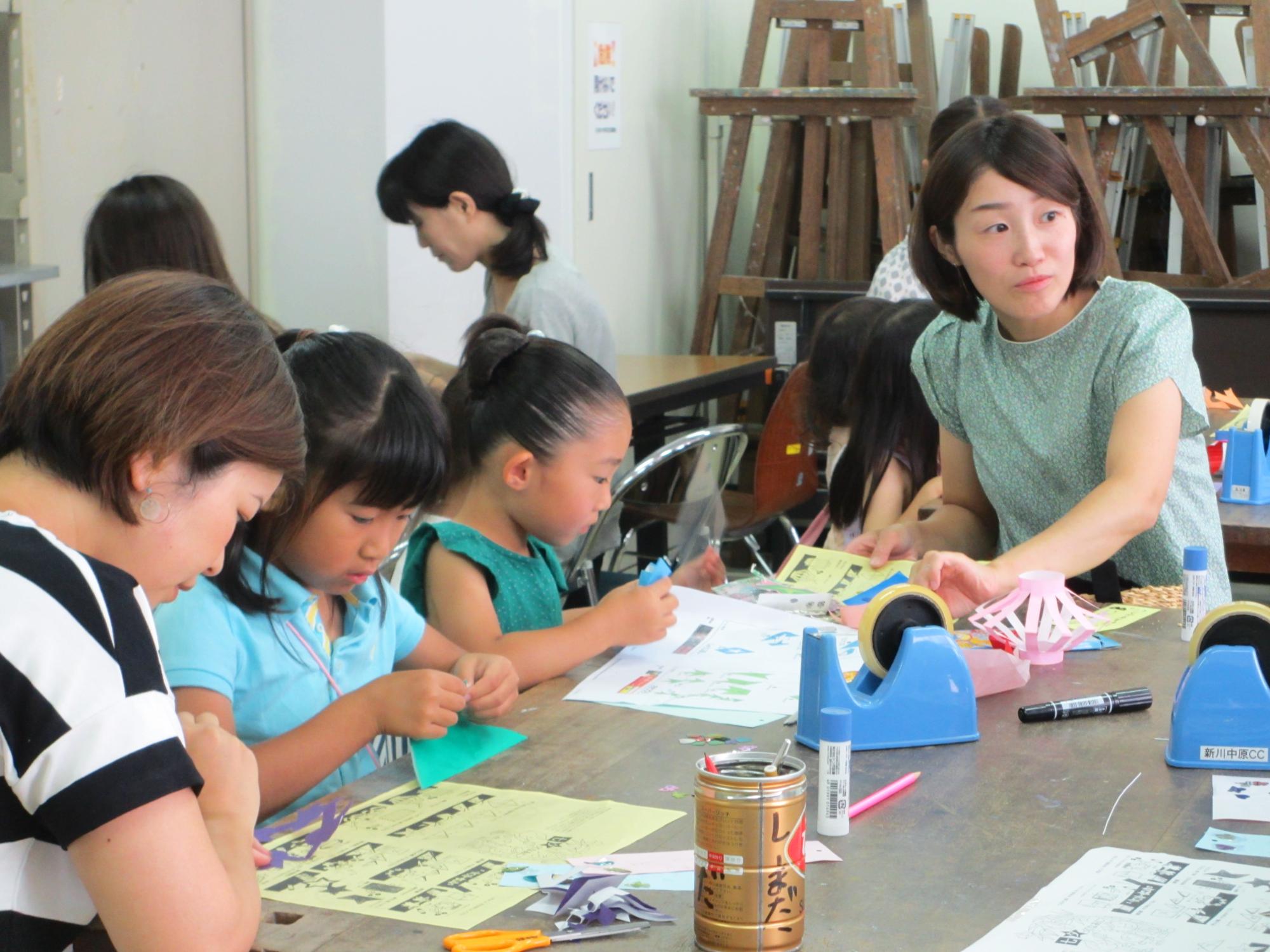二人の子供と二人の大人が紙の飾りを作っているところを近くで写した写真