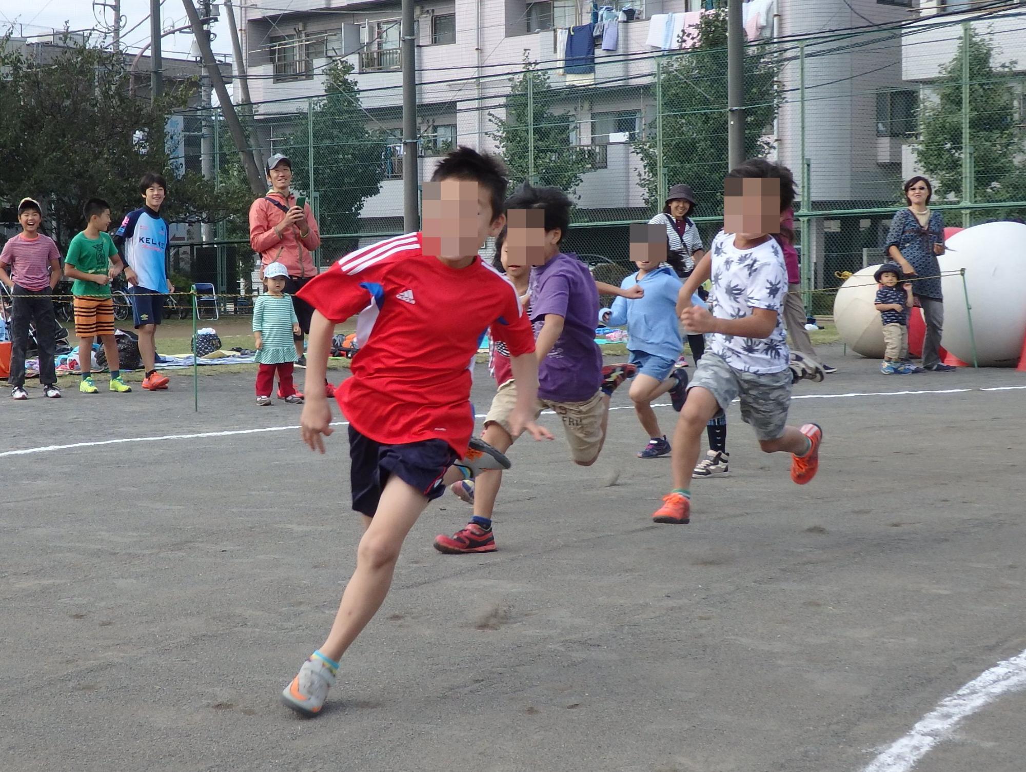 徒競走で先頭を走る赤色の服を着た子供と、追いかける三人の子供の写真