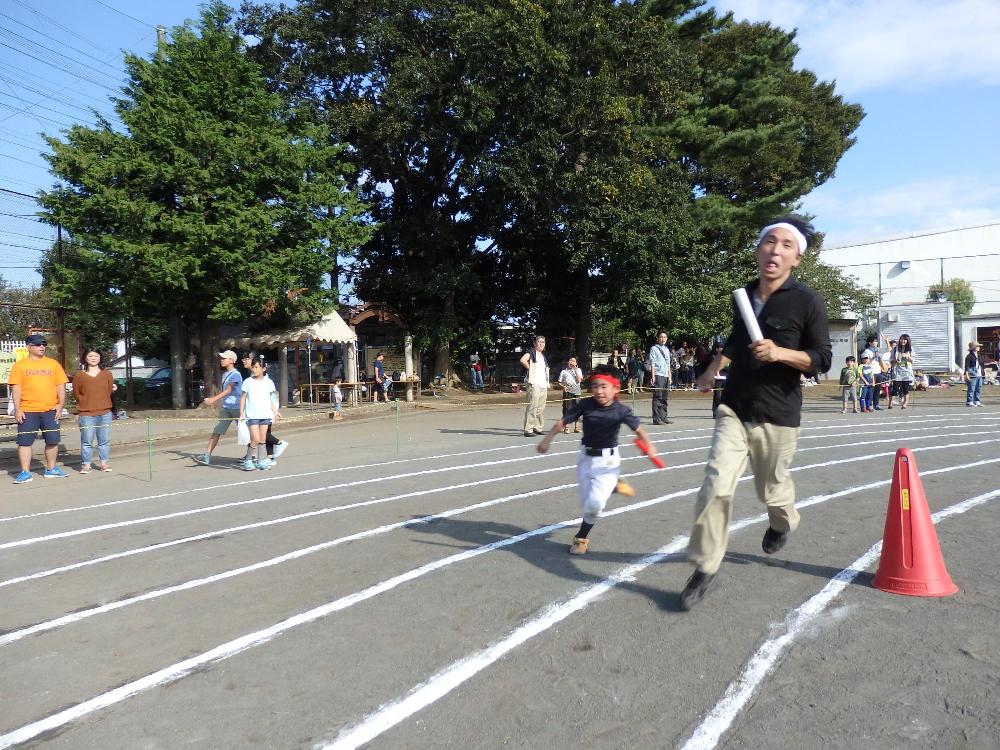 トラックを走っていく、バトンを持った大人と子供の写真