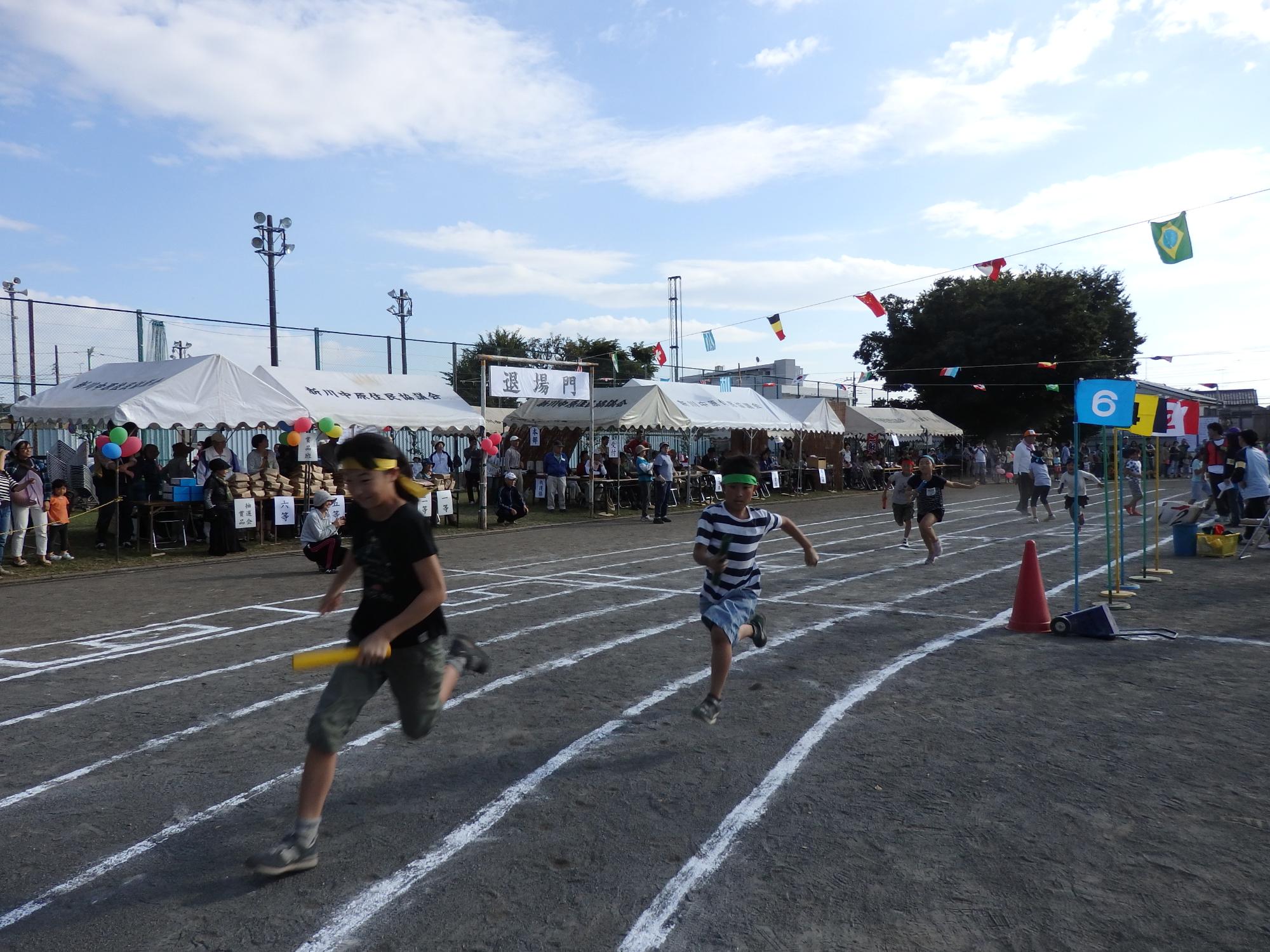 トラックを走る、バトンを持った子供と追いかけていく複数の子供の写真