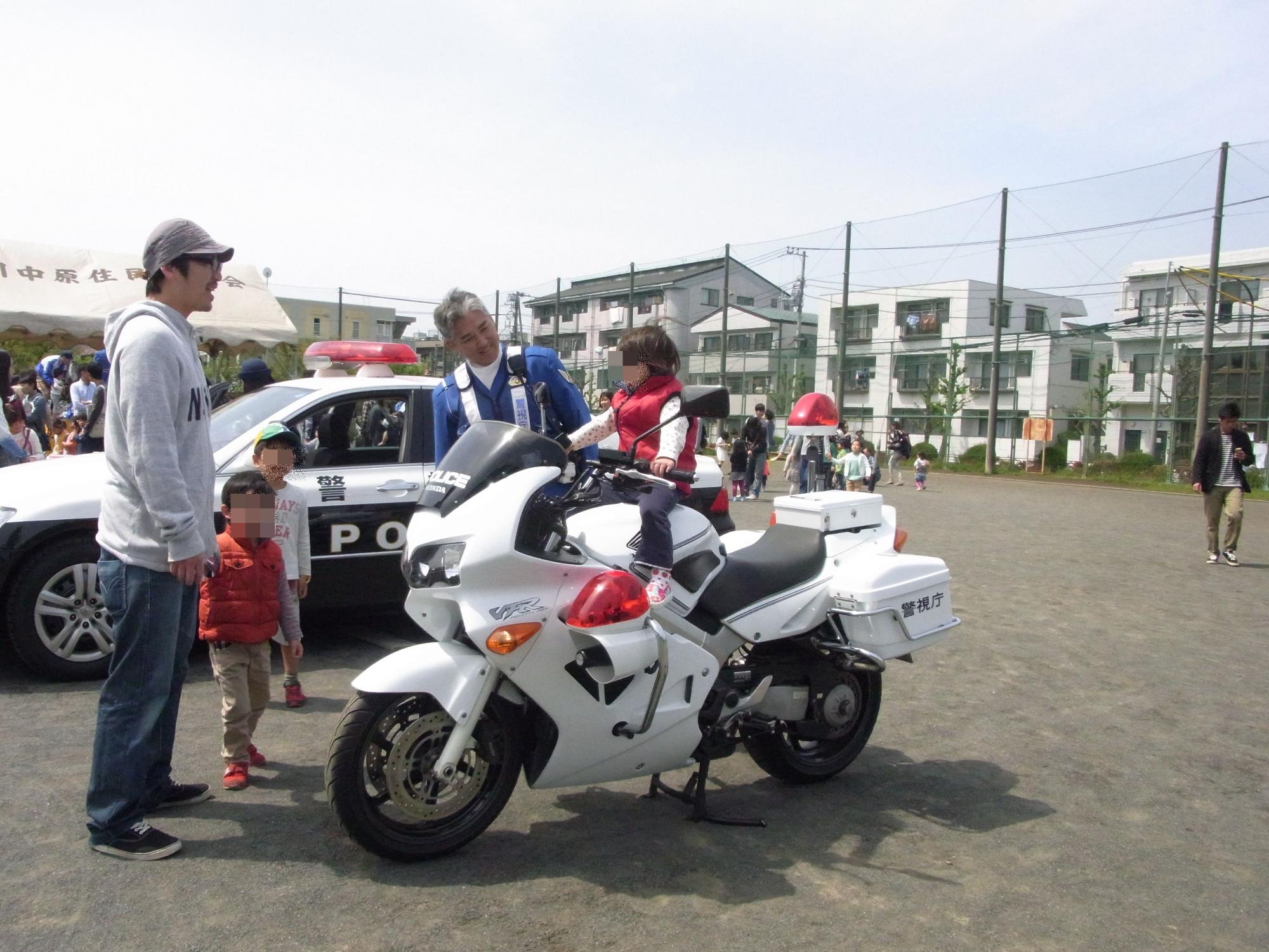 保護者と警官に見守ら得ながら、白パトカーに乗せてもらう子どもの写真