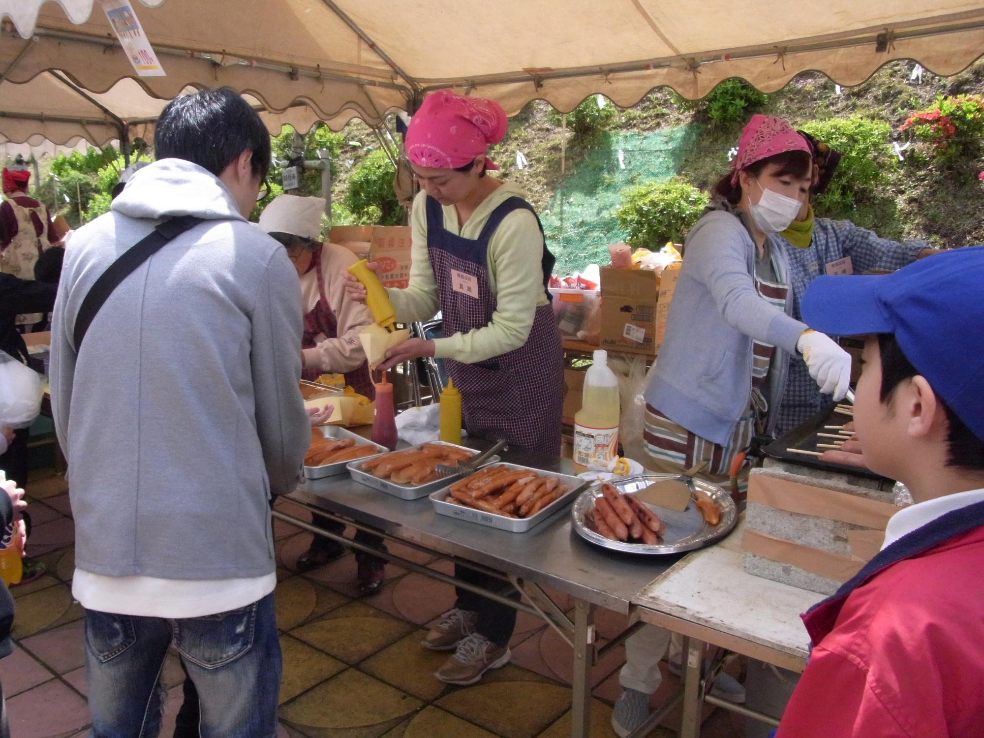 テントの中で多くのソーセージが用意され、そのうちの一つにマスタードが掛けられている写真