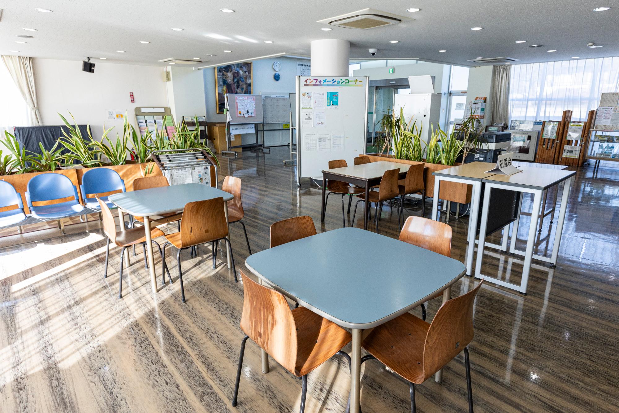 広いロビーの中央に柱を囲うインフォメーションボードがあり、コピー機と机が置かれているロビーの写真