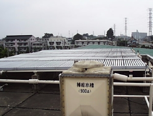 屋上に用意された、小さな補給水槽の奥にソーラーパネルが並んでいる写真
