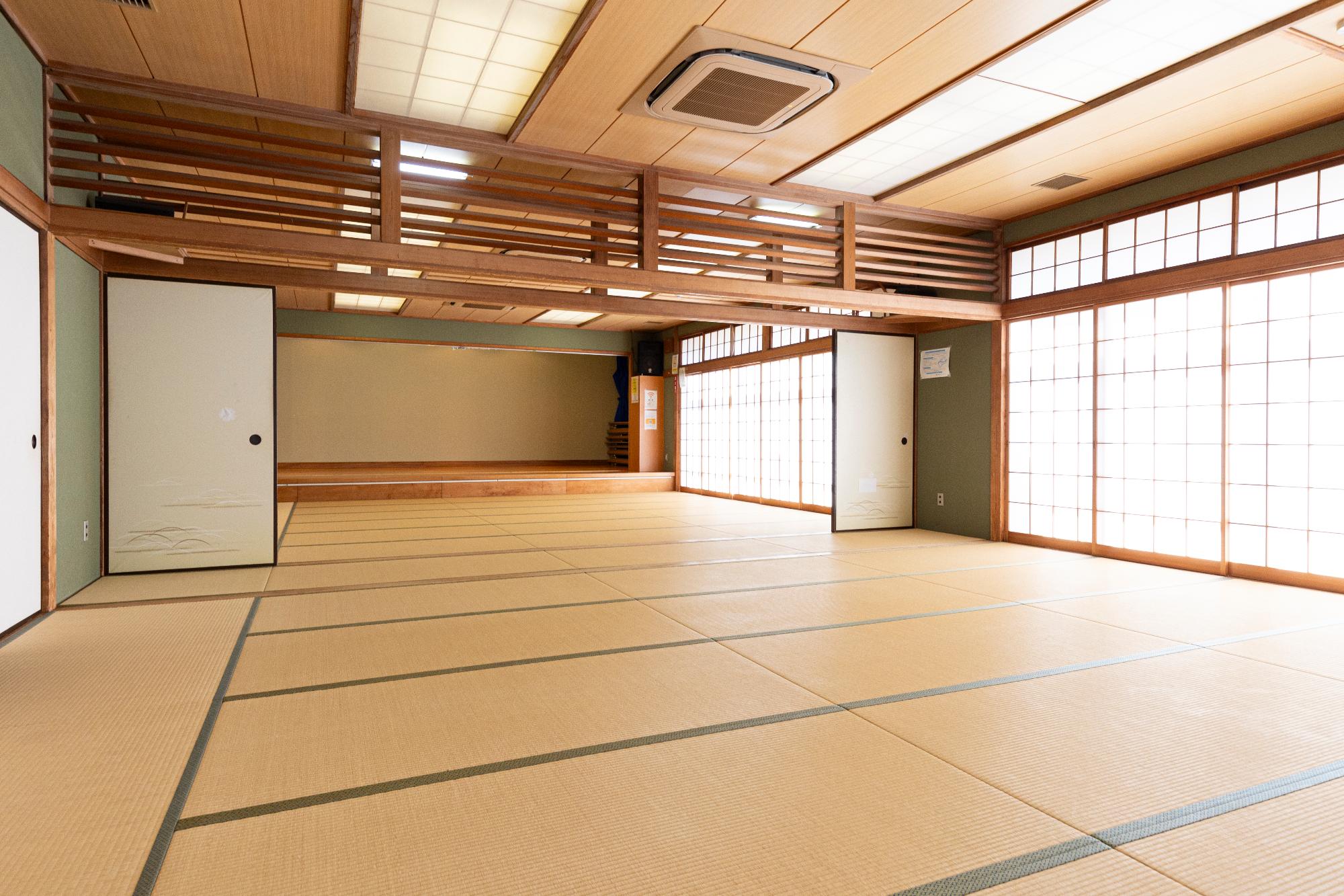 部屋の一面から光が差し込んだ50畳の和室の奥に一段上がった舞台が見える写真