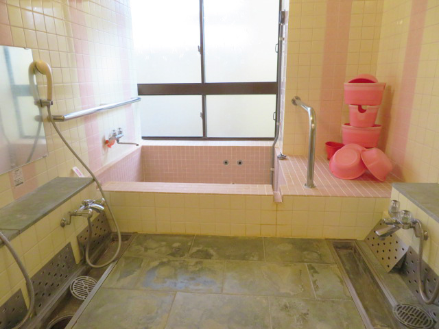 ピンク色のタイルの浴槽とピンク色の桶が置いてある浴室の写真